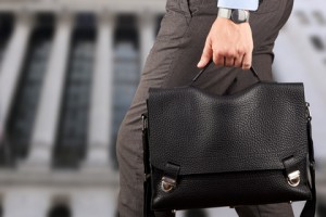 Businessman walking and holding  a  leather briefcase in his hand.  Modern city behind