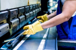 Asian worker in factory at metal skip machine putting work piece in